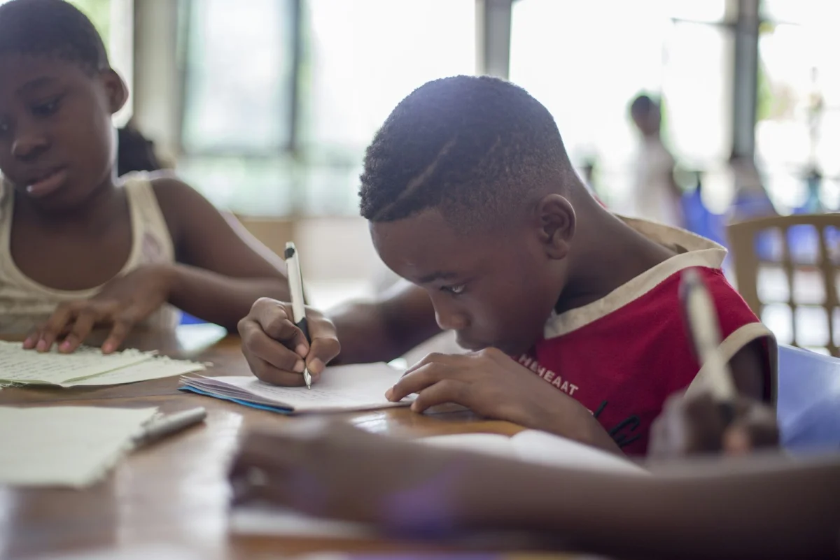 Children writing at a classroom table during a school lesson