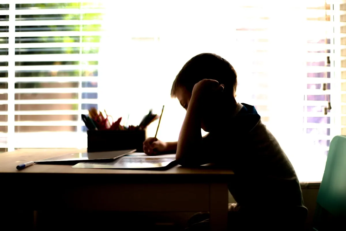 Young boy sitting at a desk writing on a piece of paper with concentration