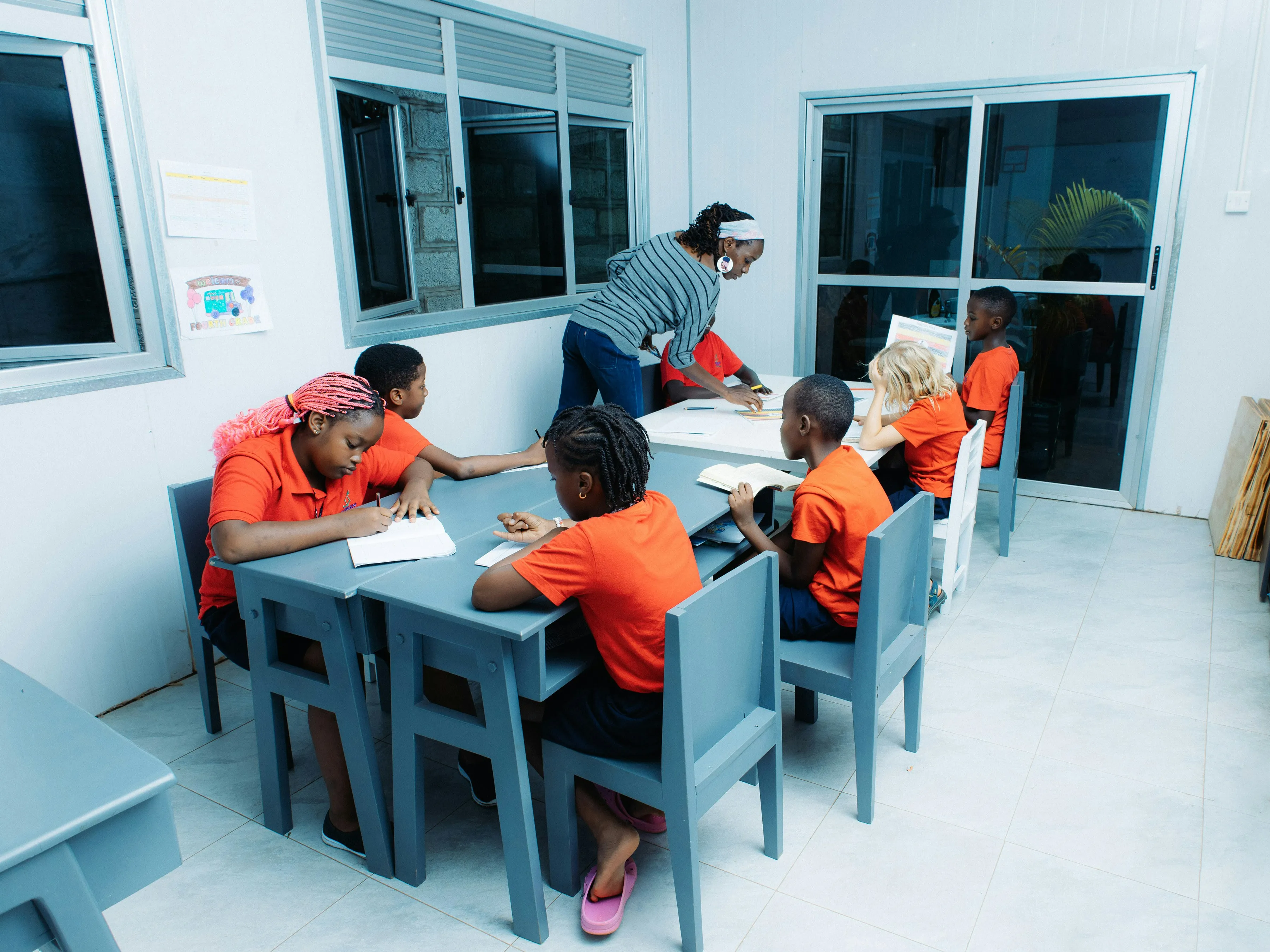 Teacher instructing children at tables in a classroom, showing a supportive educational environment.