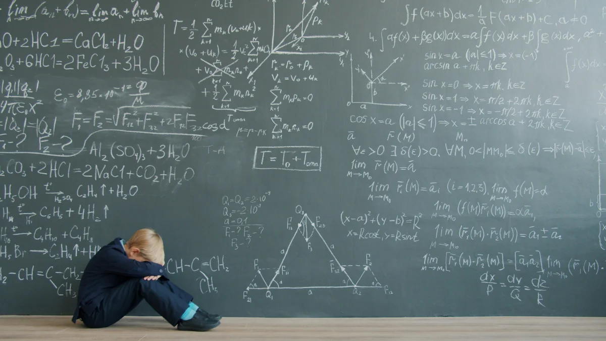 Child sitting on floor looking frustrated near chalkboard with math formulas, symbolizing emotional dysregulation and the difference between behavioral discipline and support-based intervention