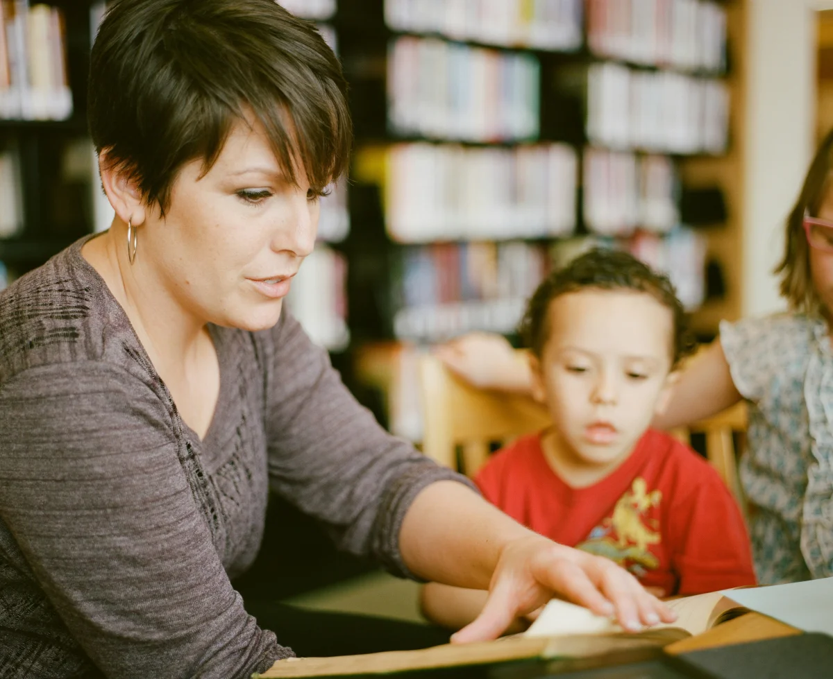 Adult supporting child's learning in library setting with books