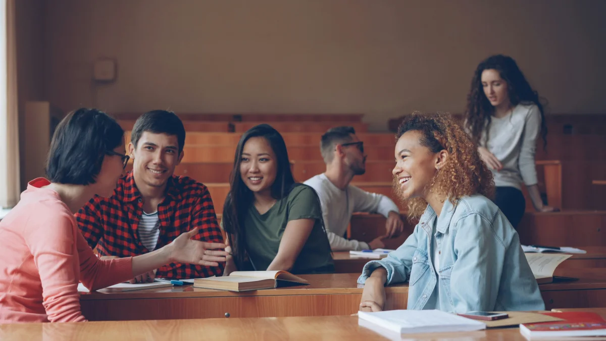 Students sitting at desks in a classroom, talking and laughing during class break