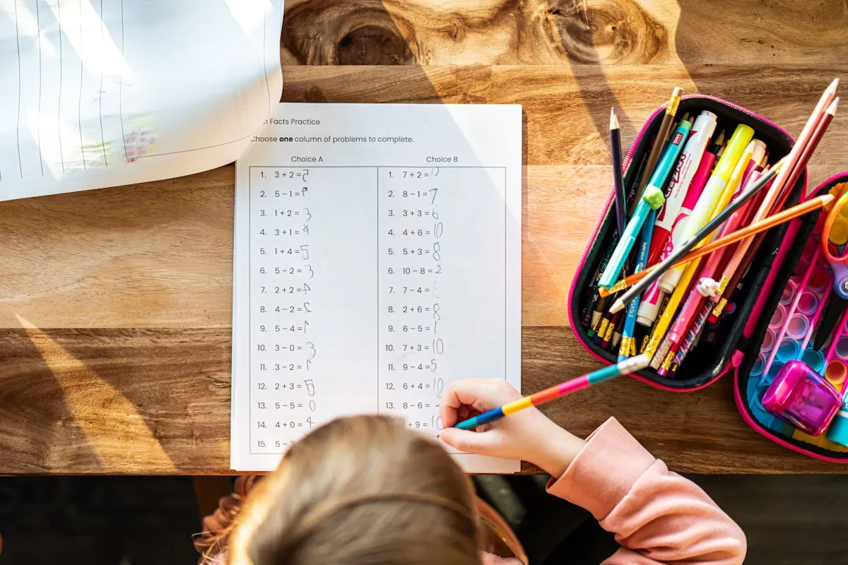 Young girl sitting at a school table with pencils and supplies
