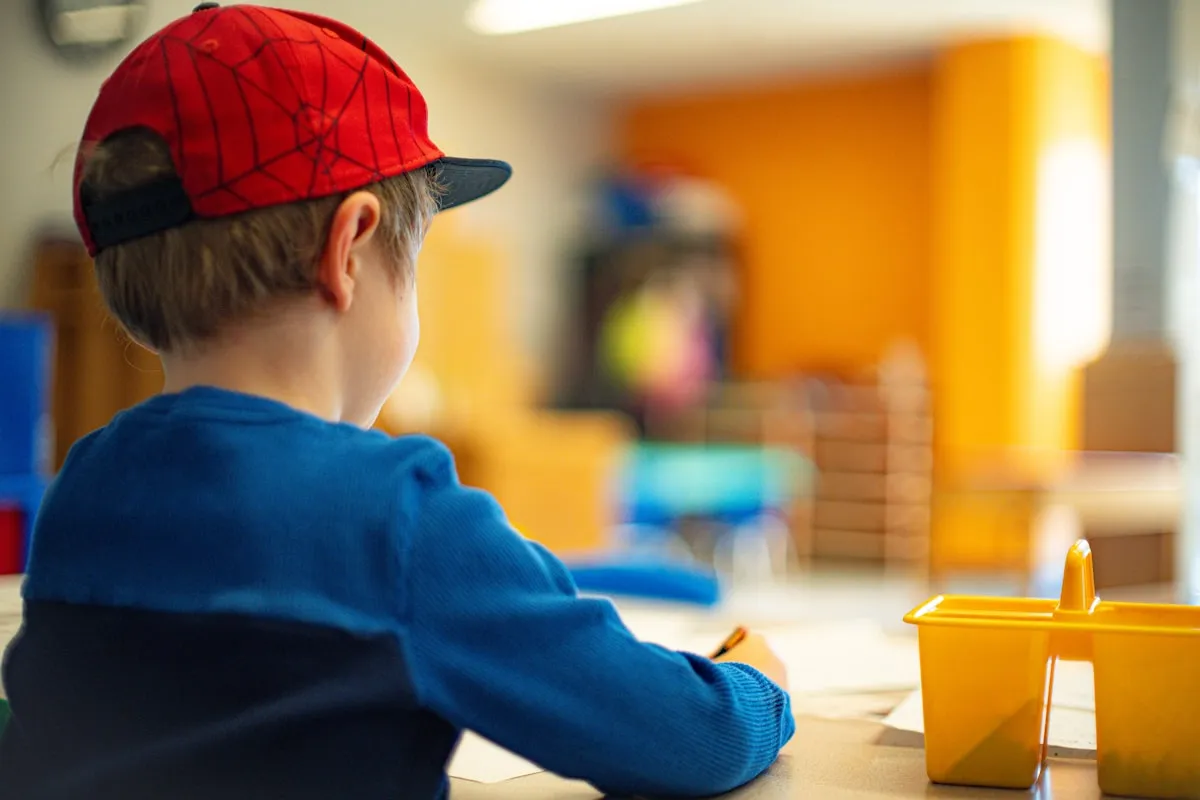 Young boy sitting at a table writing on paper in a school setting