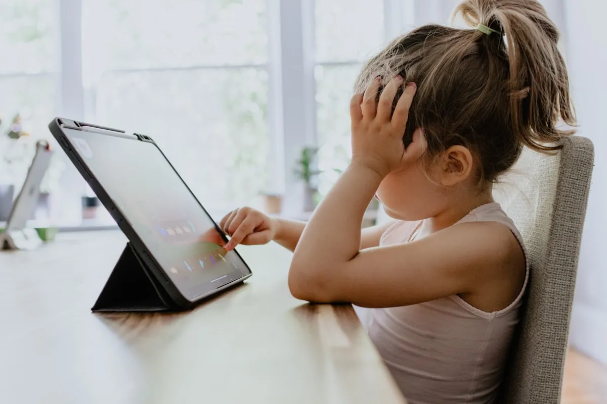 Girl in white tank top using a black tablet computer at a desk